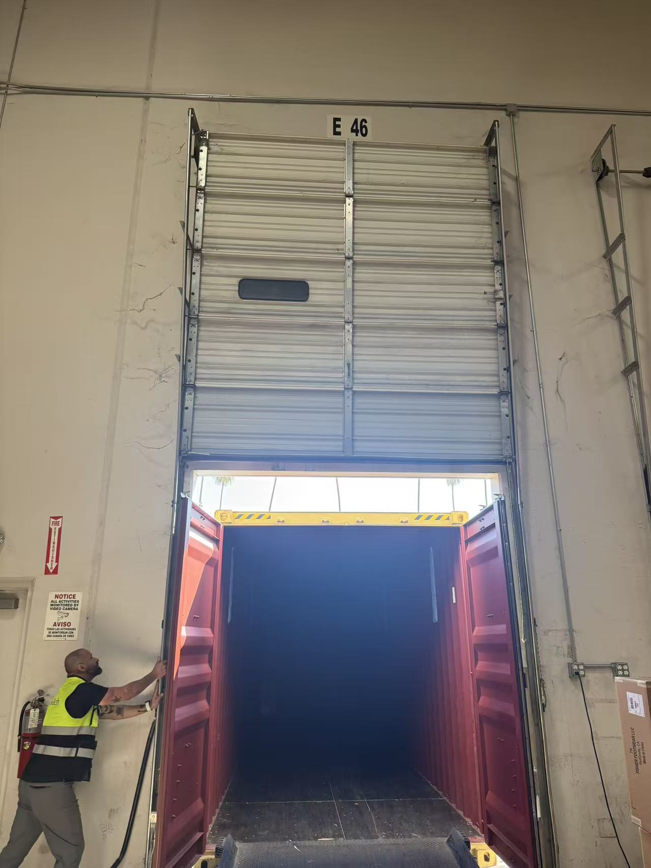 Door E46: container docked at a high-bay door, with the technician inspecting the door and opening.