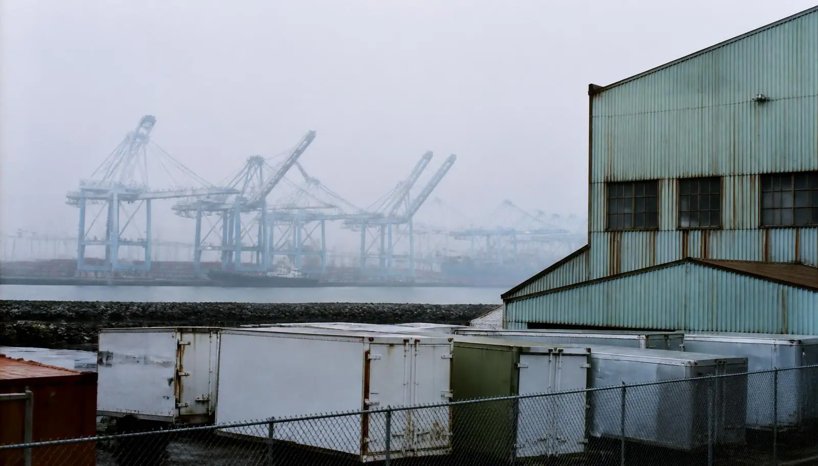Harbor-adjacent warehouse district with gantry cranes beyond the trailer yard in Long Beach CA